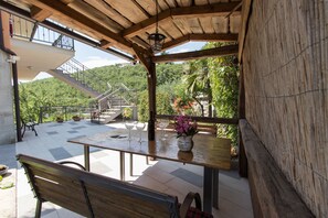 A covered outdoor patio with a wooden table, benches, and a potted plant. - Apartments Vesna (Opatija)