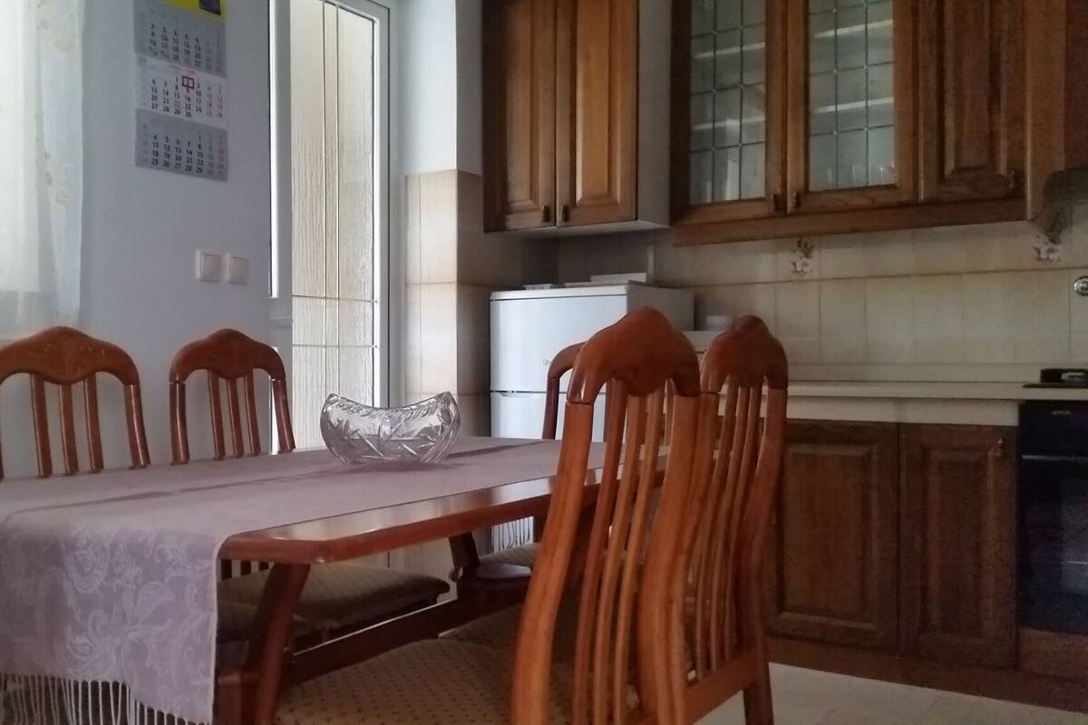 A dining area with a table, chairs, a refrigerator, and wooden cabinets.