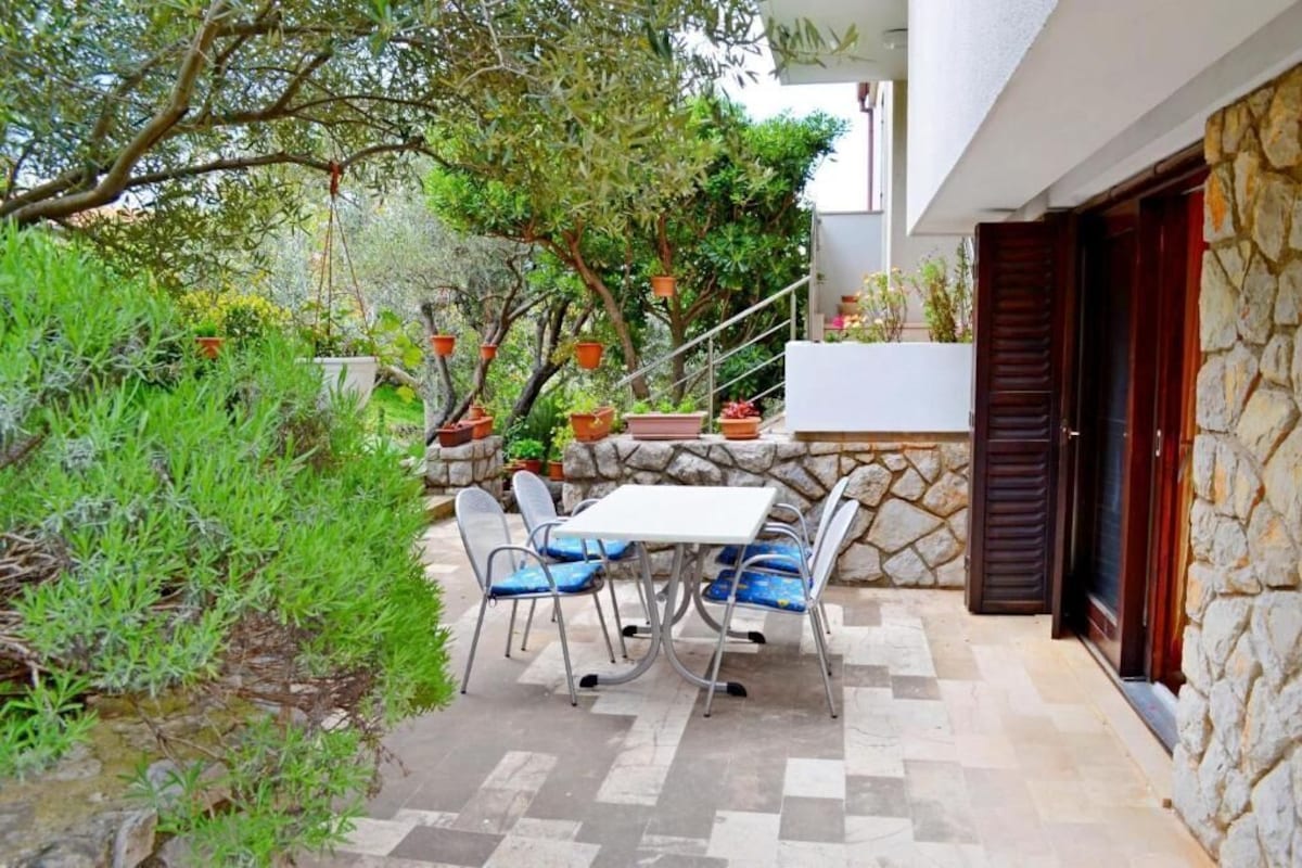 An outdoor patio with a table and chairs, surrounded by potted plants and a stone wall.
