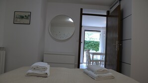 A hotel room with a bed, a round mirror, a framed picture, and a view of an outdoor area with a table and chairs. - Apartments Marija (Cres)