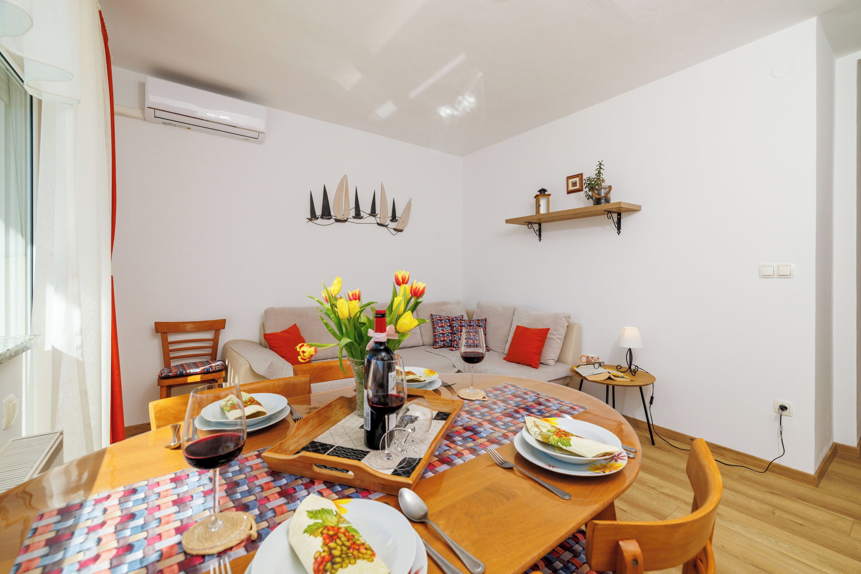 A dining area with a wooden table set for a meal, a vase with flowers, and a wall-mounted air conditioner.