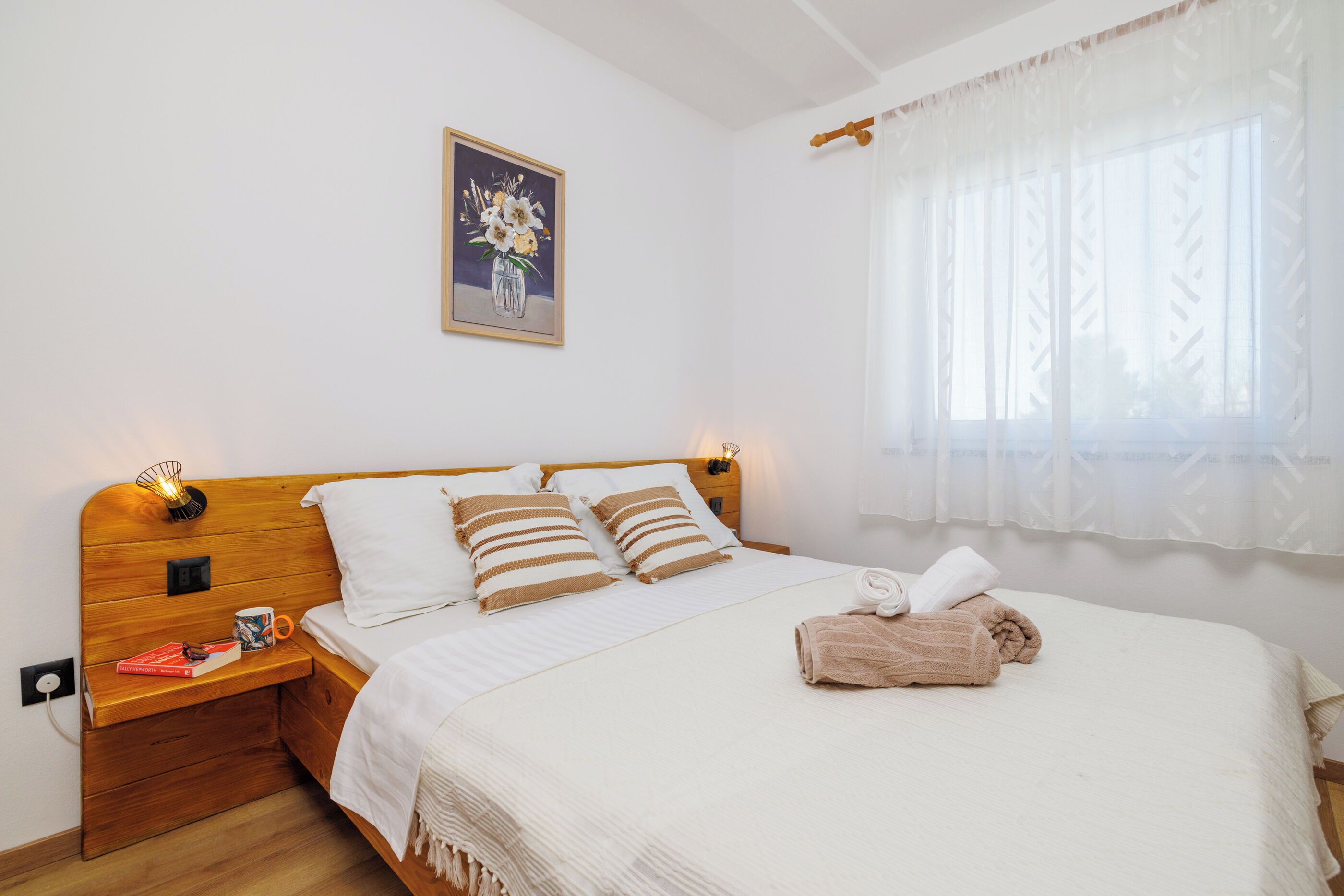 A neatly made bed with a white and brown striped pillow, a wooden headboard, and a small bedside table with a book and a mug.