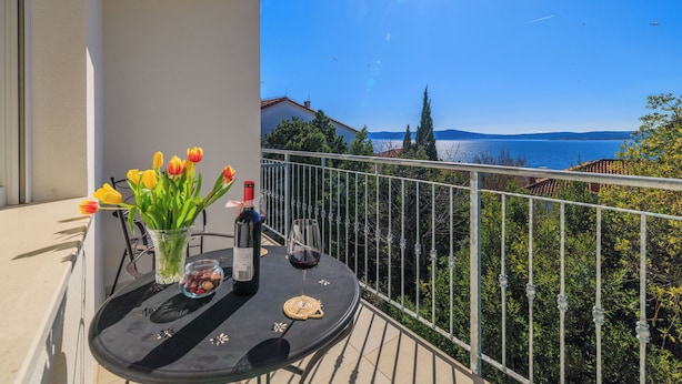 A balcony with a table, a vase of flowers, a bottle of wine, and a glass of wine. - Apartments Iva (Crikvenica)