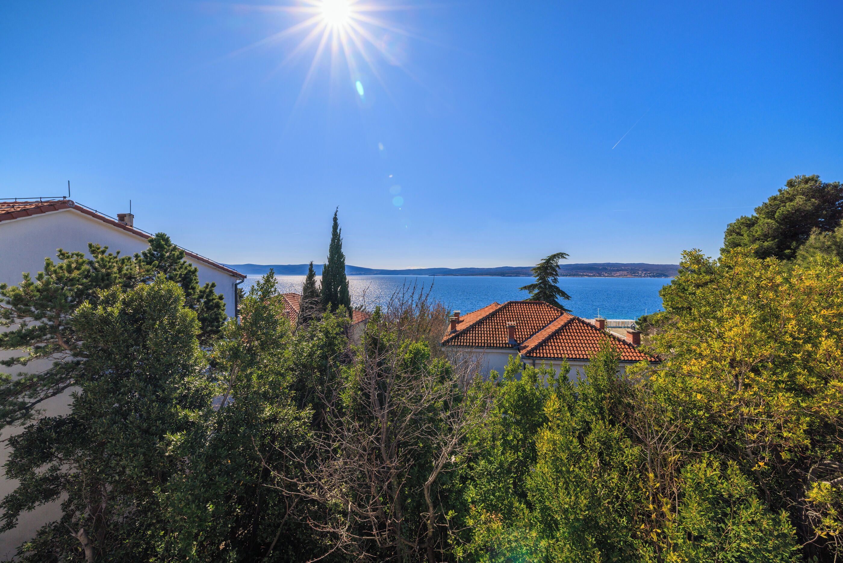 A coastal view with a clear sky, a body of water, and buildings with red-tiled roofs.