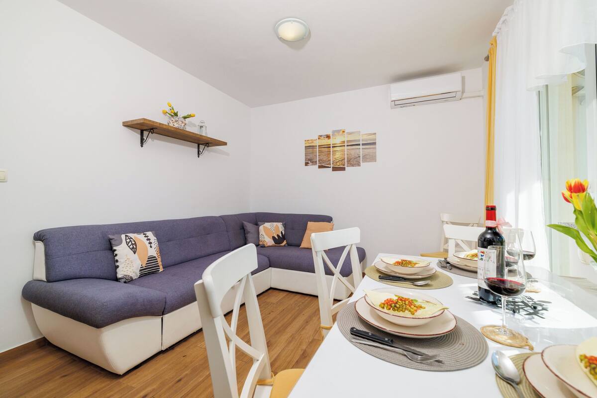 A modern living room with a sofa, dining table, chairs, and a small shelf with flowers.