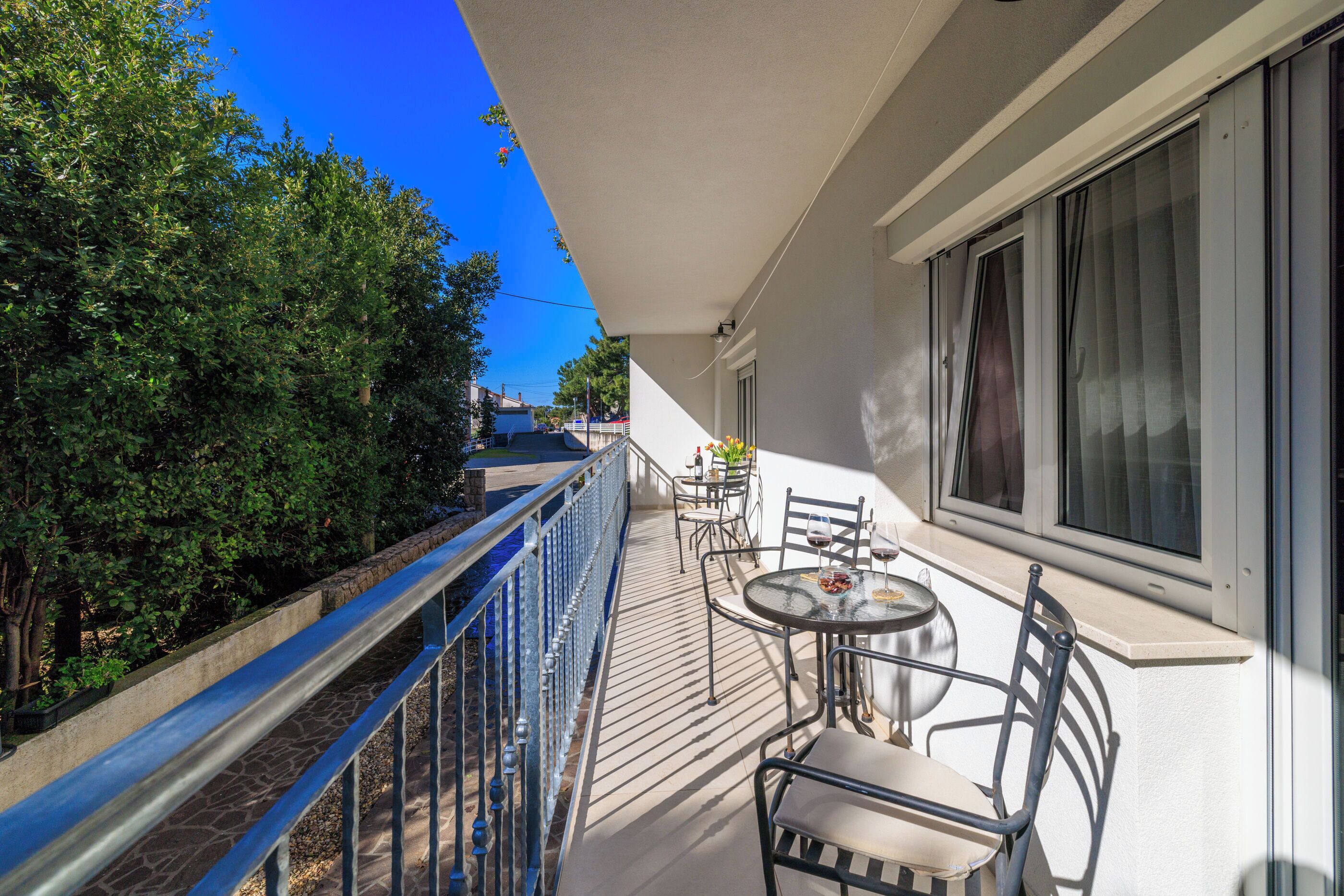 Un balcon avec une table et des chaises, une balustrade et une vue sur des arbres et un immeuble.