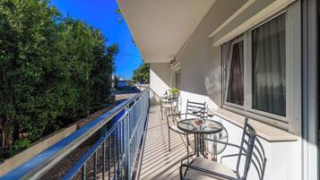 Un balcon avec une table et des chaises, une balustrade et une vue sur des arbres et un immeuble.