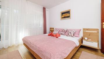 Una cama bien hecha con un edredón rosa, una mesita de noche con una taza, y un cuadro en la pared.