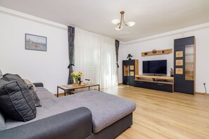 A modern living room with a grey sofa, wooden flooring, a TV, and a decorative plant.