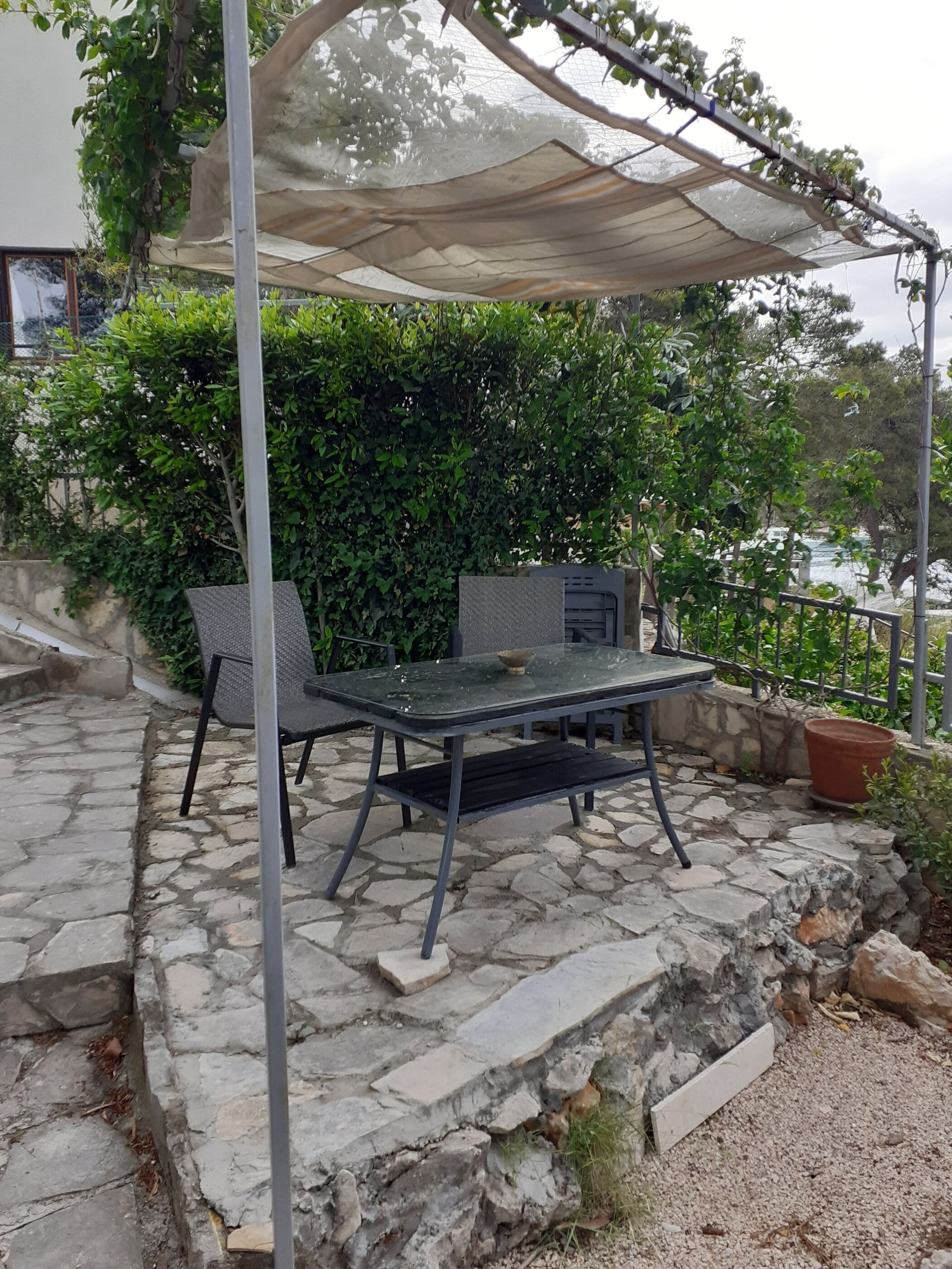 An outdoor patio with a table and chairs, a pergola providing shade, and a view of a rocky landscape and greenery.