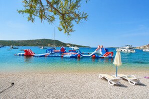A beach with clear water, boats, and inflatable play structures. - Apartment Roje (Primosten)