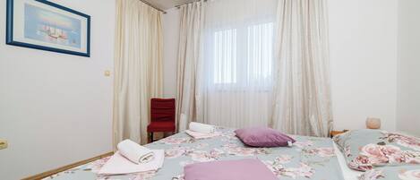 A bedroom with two beds, floral bedding, a red chair, and a painting on the wall.