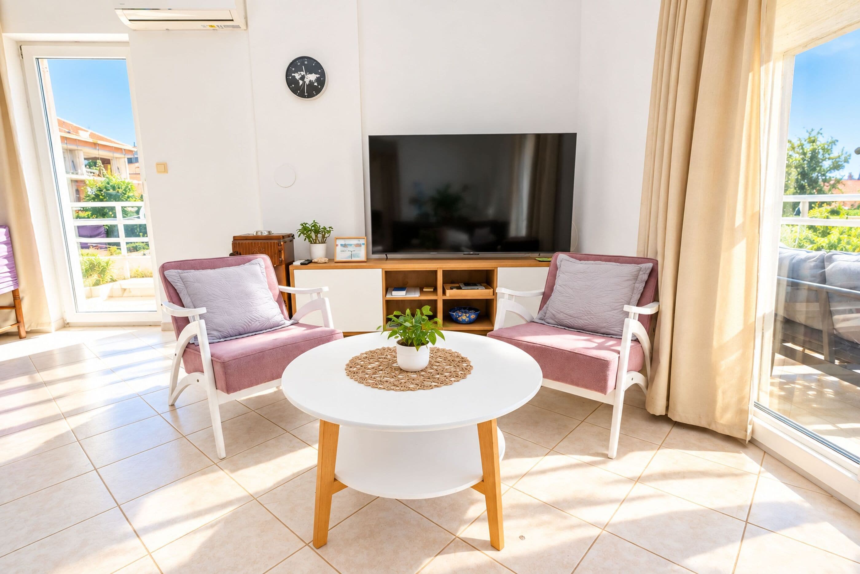 Un salon moderne avec un téléviseur à écran plat, deux fauteuils, une table basse ronde et une plante en pot.