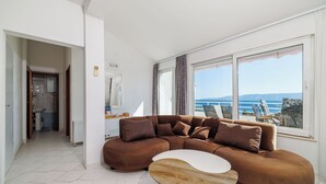 A modern living room with a large brown sectional sofa, a wooden coffee table, and a view of the sea through large windows.