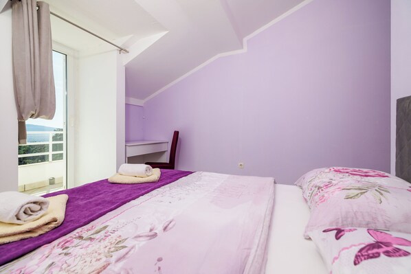 Un dormitorio con pared morada, cama con ropa de cama floral, ventana con cortinas y vista al exterior.