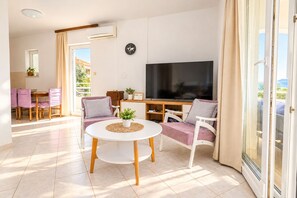 A modern living room with a flat-screen TV, a round white table, and a sofa with cushions.