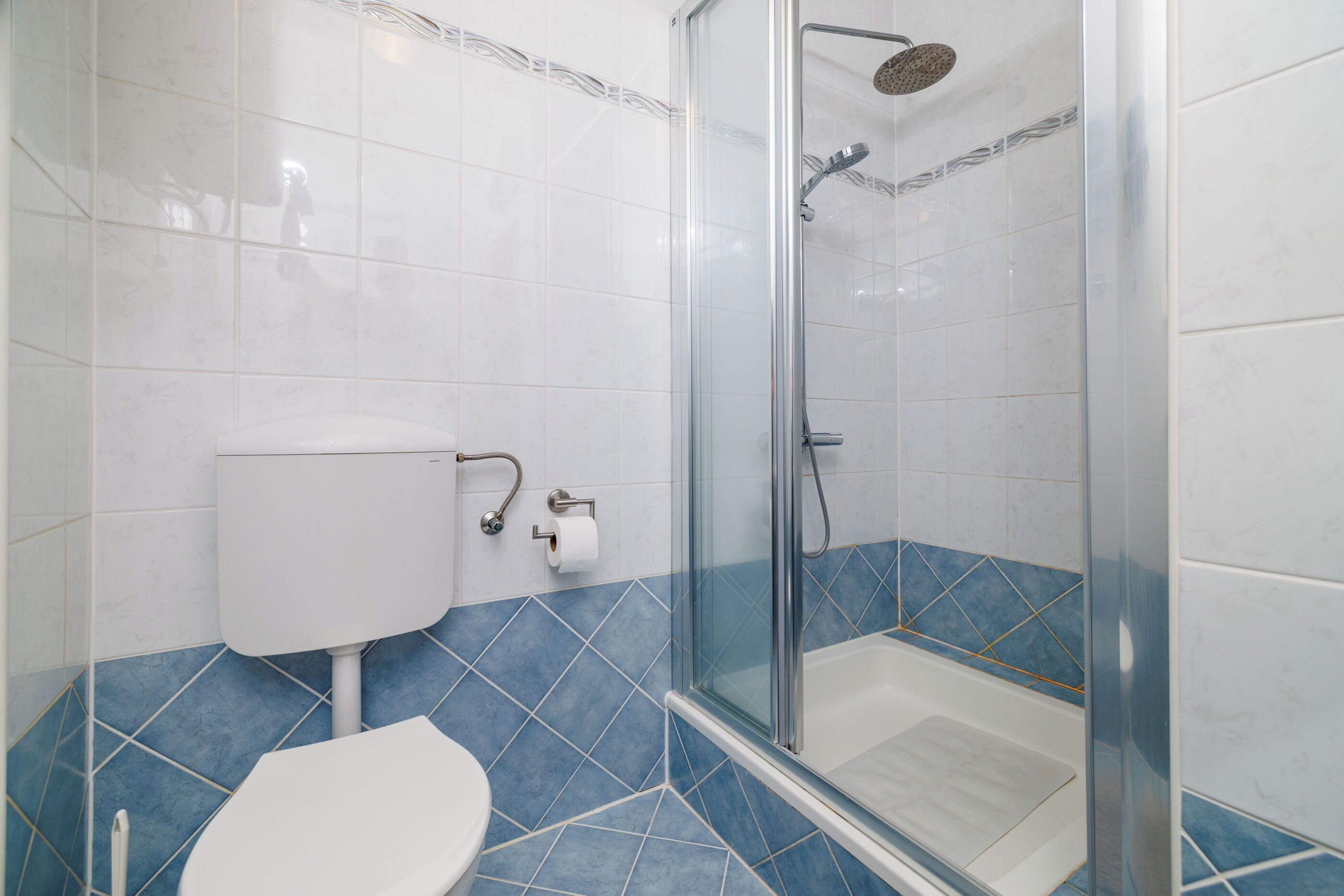 Une salle de bain avec des toilettes, une douche en verre et des murs recouverts de carreaux bleus.