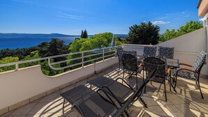 A terrace with a table and chairs, overlooking a body of water and greenery.