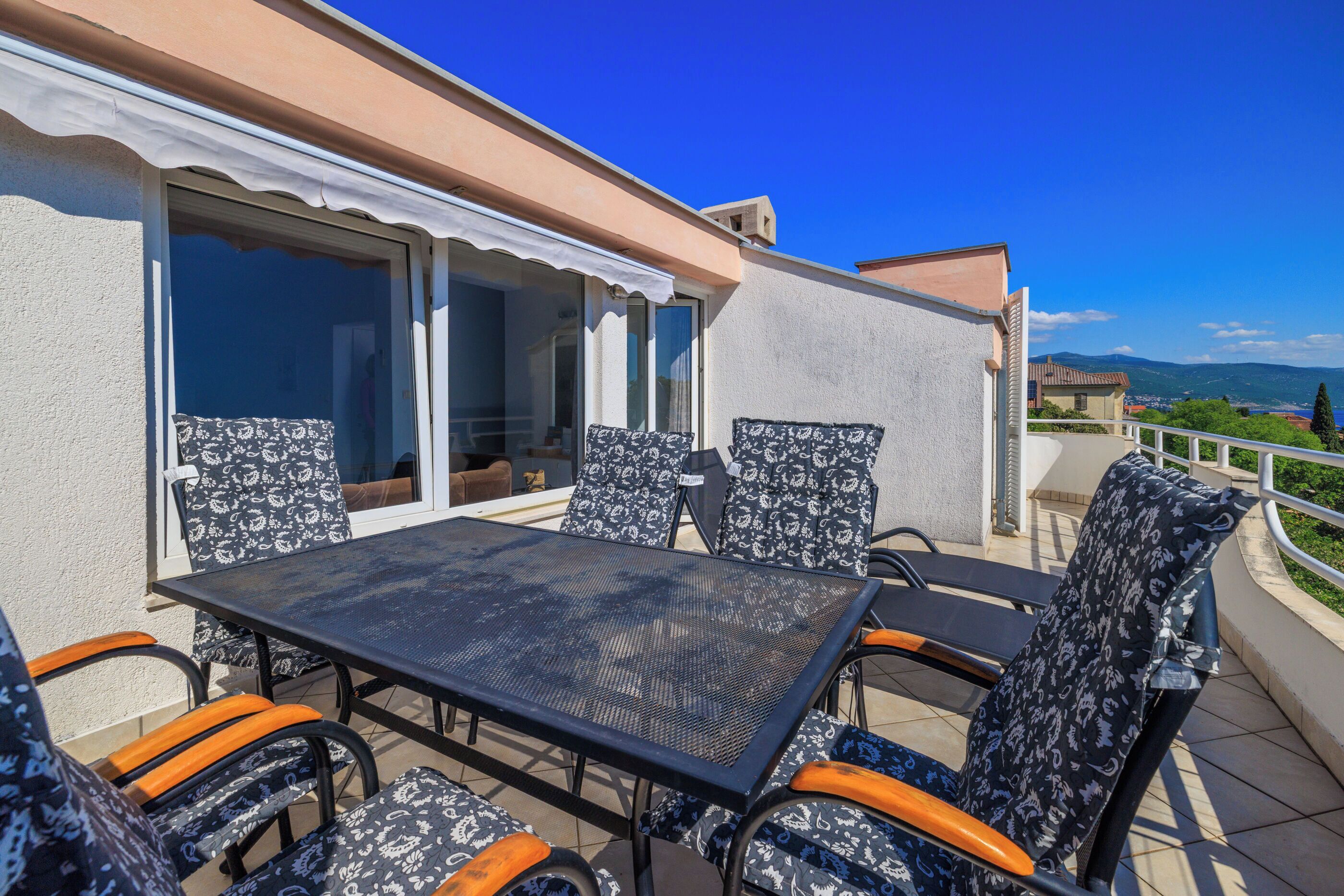 An outdoor patio with a table and chairs, a sliding glass door, and a view of the landscape.