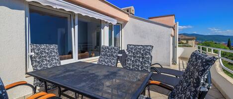 An outdoor patio with a table and chairs, a sliding glass door, and a view of the landscape.
