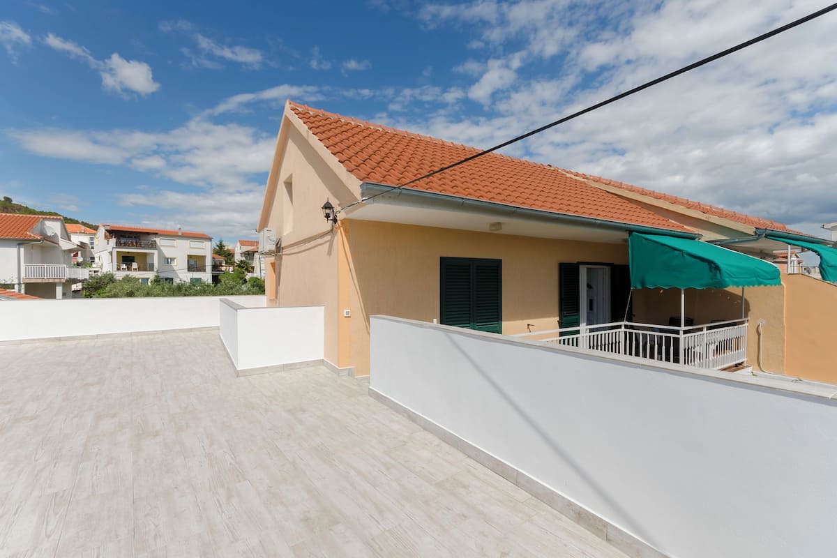 A residential building with a red-tiled roof, a balcony with a green awning, and a white exterior wall.
