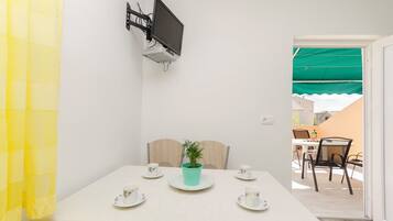 Un coin repas avec une table dressée pour quatre personnes, une plante en pot et un téléviseur fixé au mur.