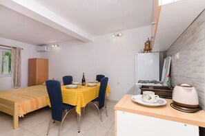 A small, well-lit room with a bed, a dining table with chairs, a kitchenette, and a window with curtains. - Apartments Mila II (Tribunj)