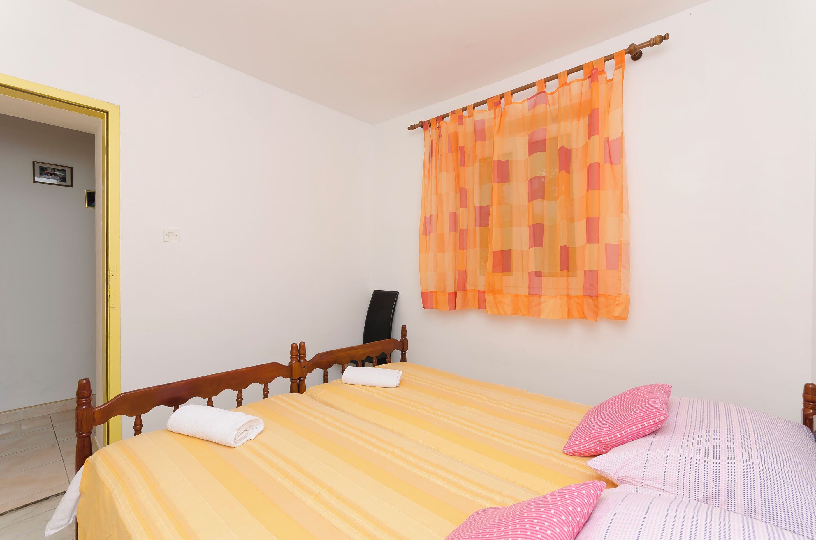 Un dormitorio con cama, almohadas, cabecero de madera, cortina y una silla.
