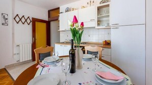 A dining area with a table set for four, a vase with flowers, and a kitchen in the background. - Apartments Ivana (Crikvenica)