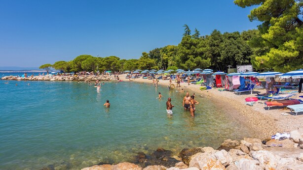 A beach with clear water, people swimming, and beach umbrellas. - Apartments Ivana (Crikvenica)