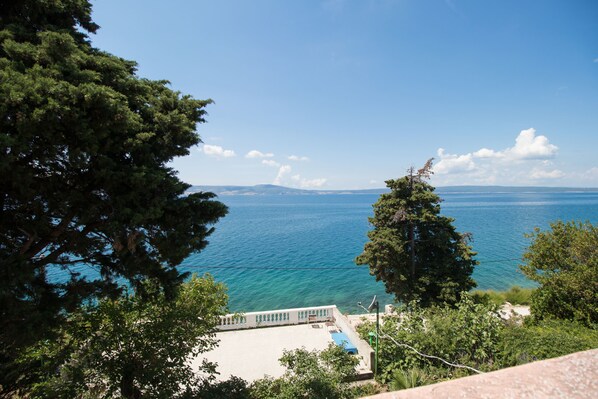 A coastal view with a clear sky, a pool area, and a distant shoreline. - Apartments Josip by the sea (Novi Vinodolski)