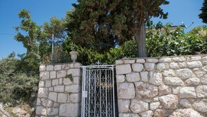 A stone wall with a metal gate, surrounded by trees and vegetation. - Apartments Josip by the sea (Novi Vinodolski)