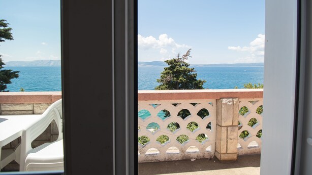 A balcony with a view of the sea and mountains, white plastic chairs, and a decorative fence. - Apartments Josip by the sea (Novi Vinodolski)