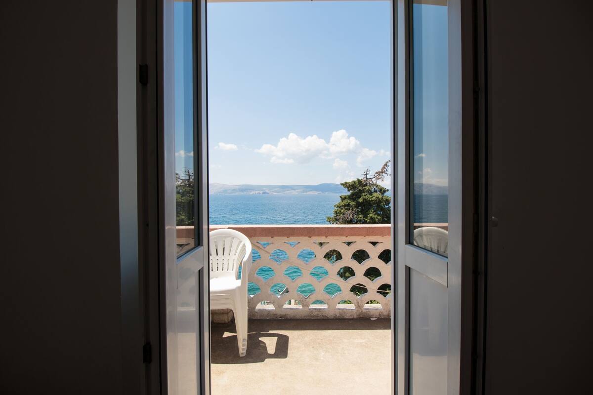 Un balcón con vista al mar, una silla blanca y una barandilla decorativa.