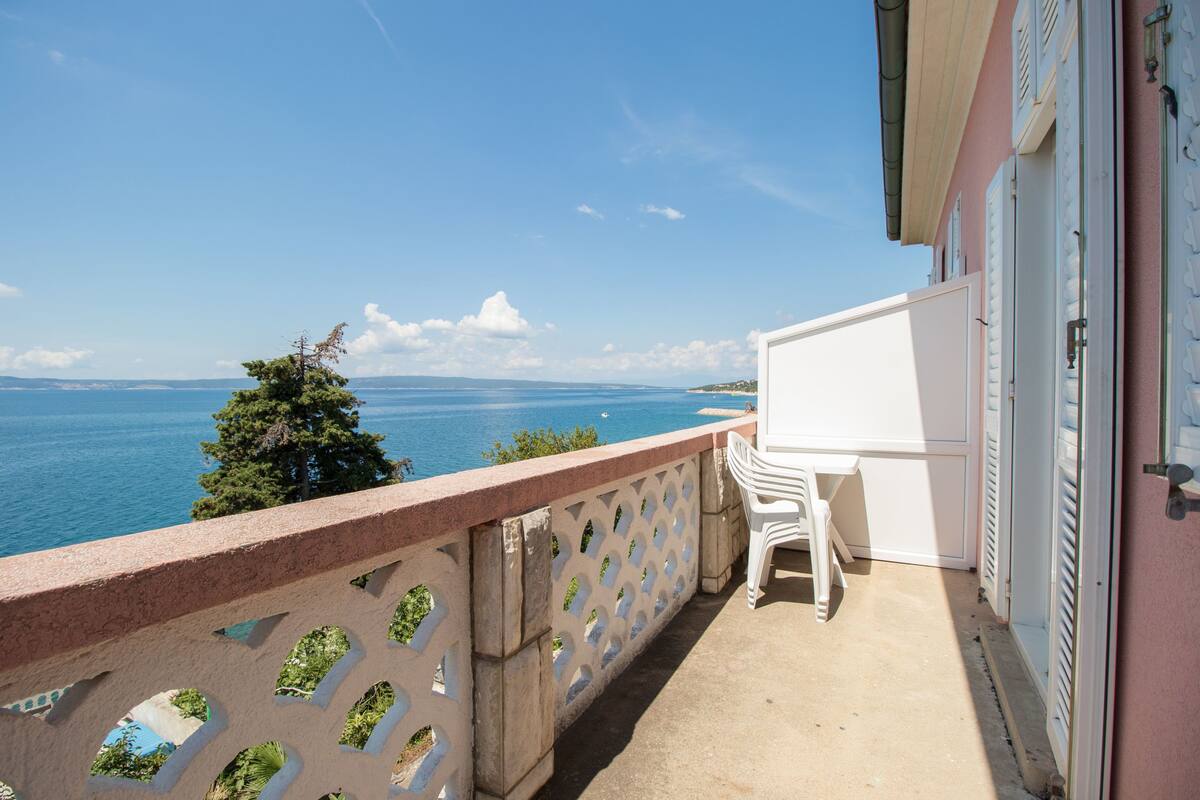 Un balcón con vista al mar, una silla blanca y una puerta blanca.