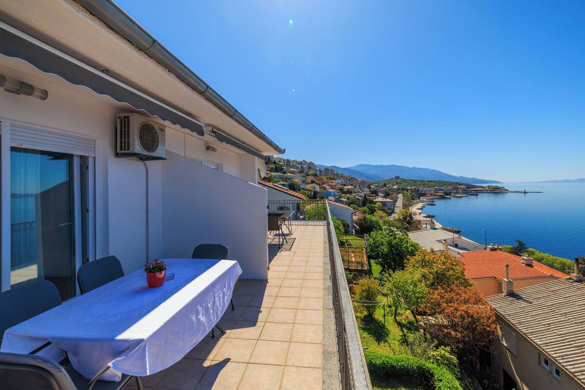 Un balcón con mesa y sillas, con vista a un pueblo costero y al mar.