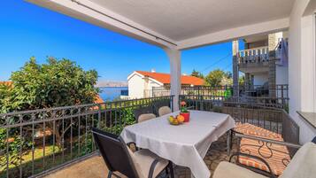 A balcony with a table set for two, outdoor seating, and a view of the sea and buildings.