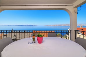 Un balcon avec une table dressée pour deux personnes, offrant une vue sur une étendue d’eau et sur la terre ferme au loin.