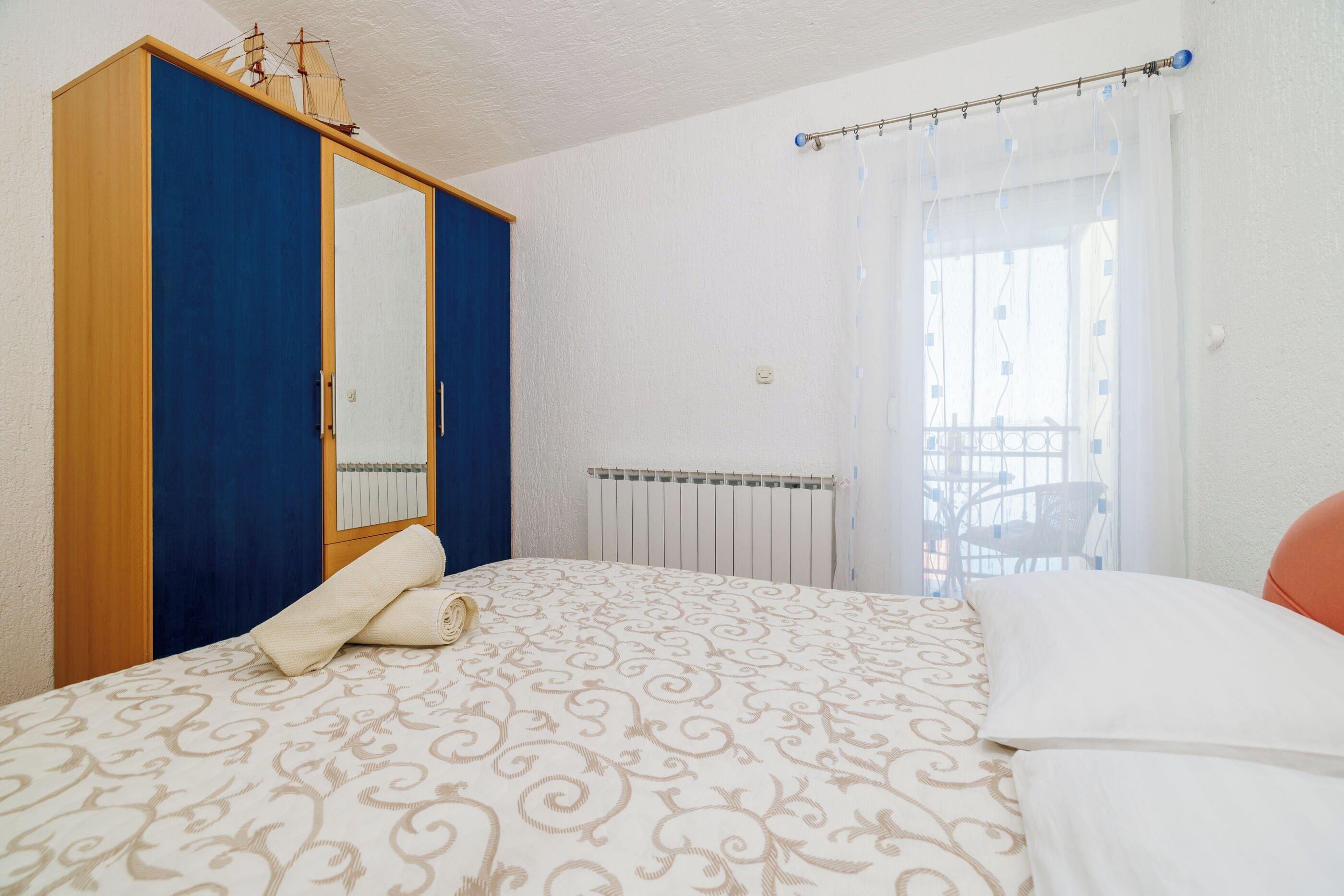 A bedroom with a bed, a wardrobe, a radiator, and a window with curtains.