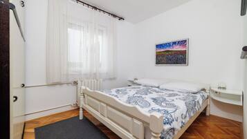 Un dormitorio con cama, mesita de noche, un cuadro y ventana con cortinas.