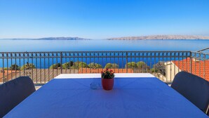 A balcony with a table and chairs, overlooking a calm sea and distant hills.
