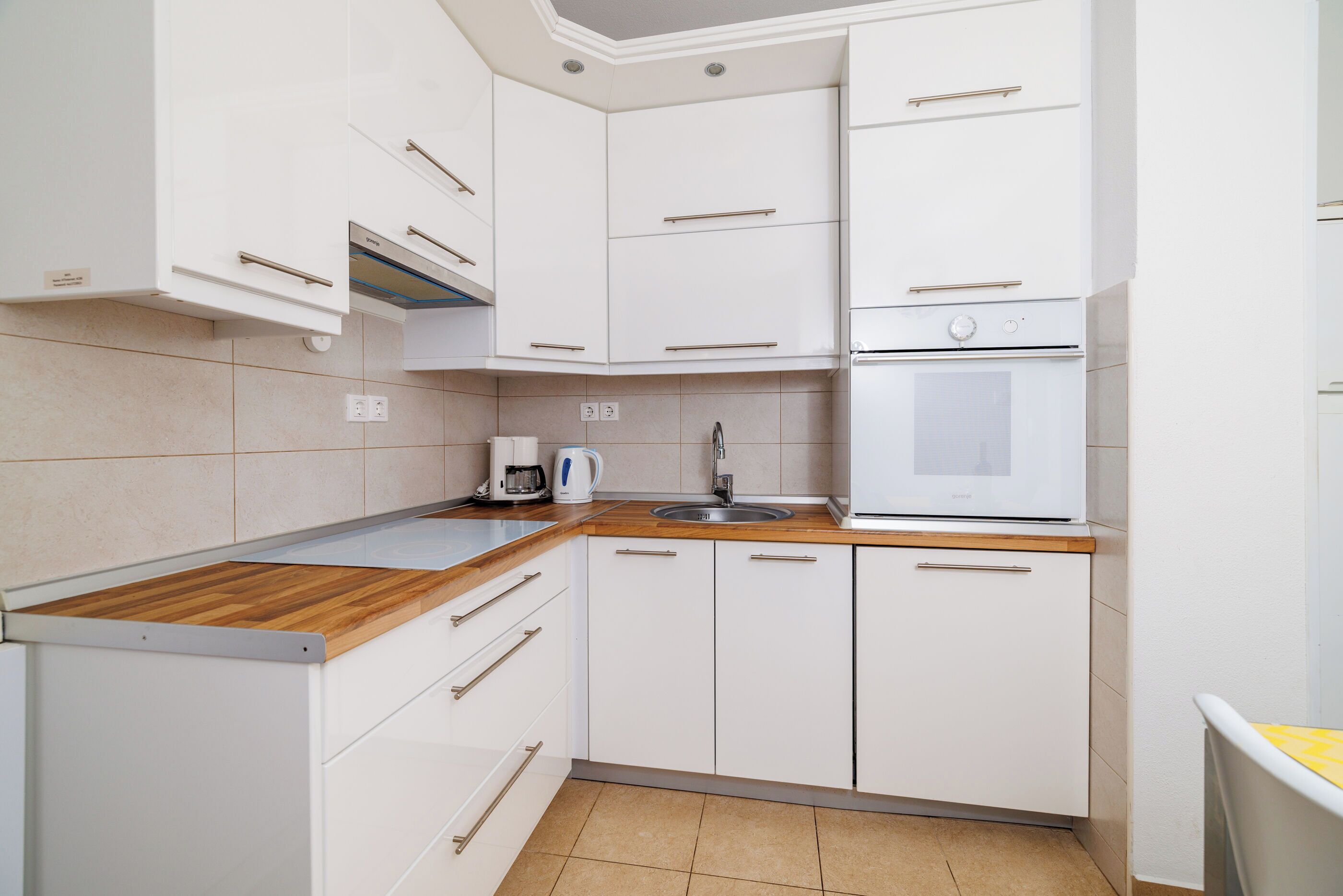 A modern kitchen with white cabinets, a wooden countertop, a built-in oven, and a sink.