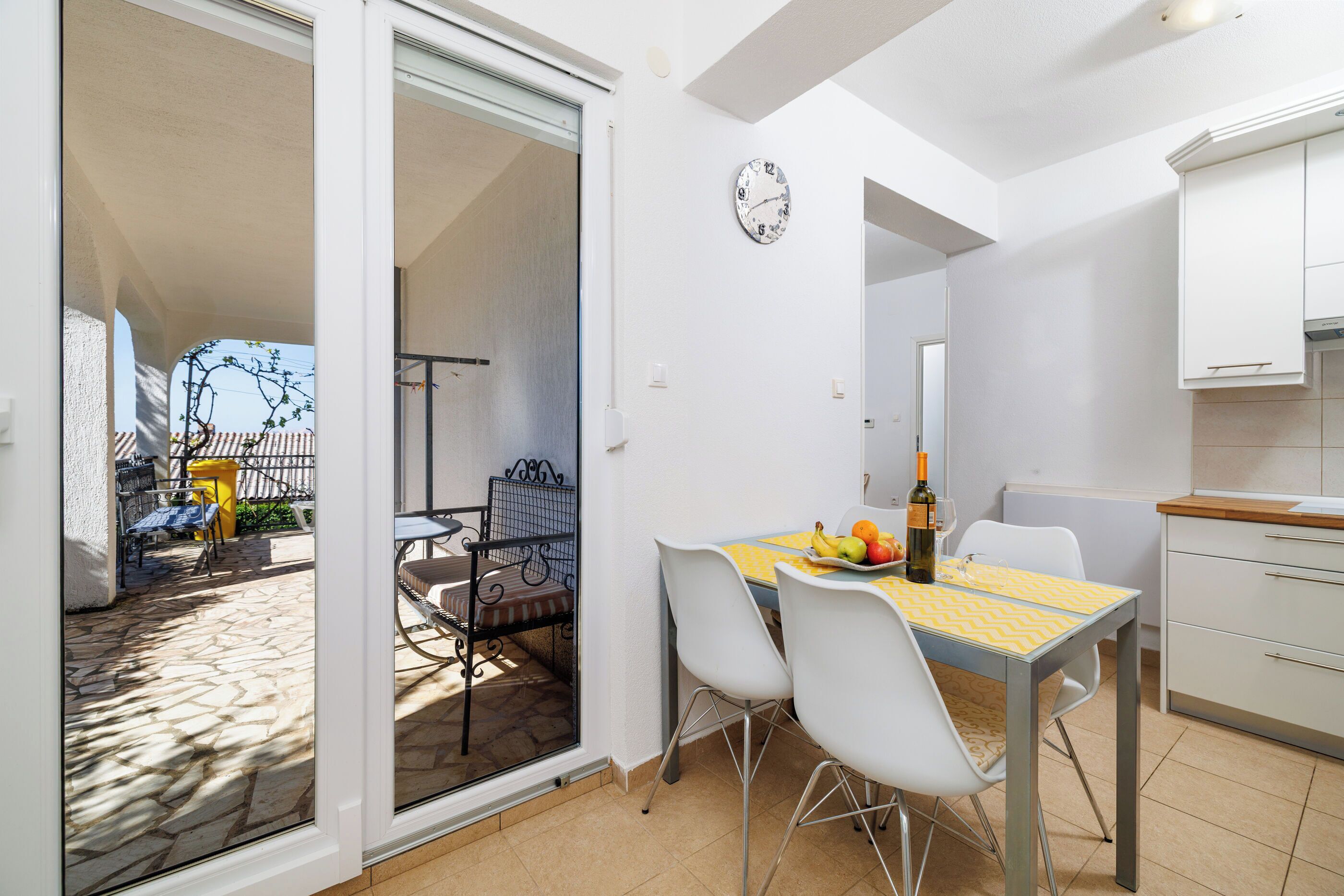 A dining area with a table set for two, a clock on the wall, and a view of the outdoor patio.