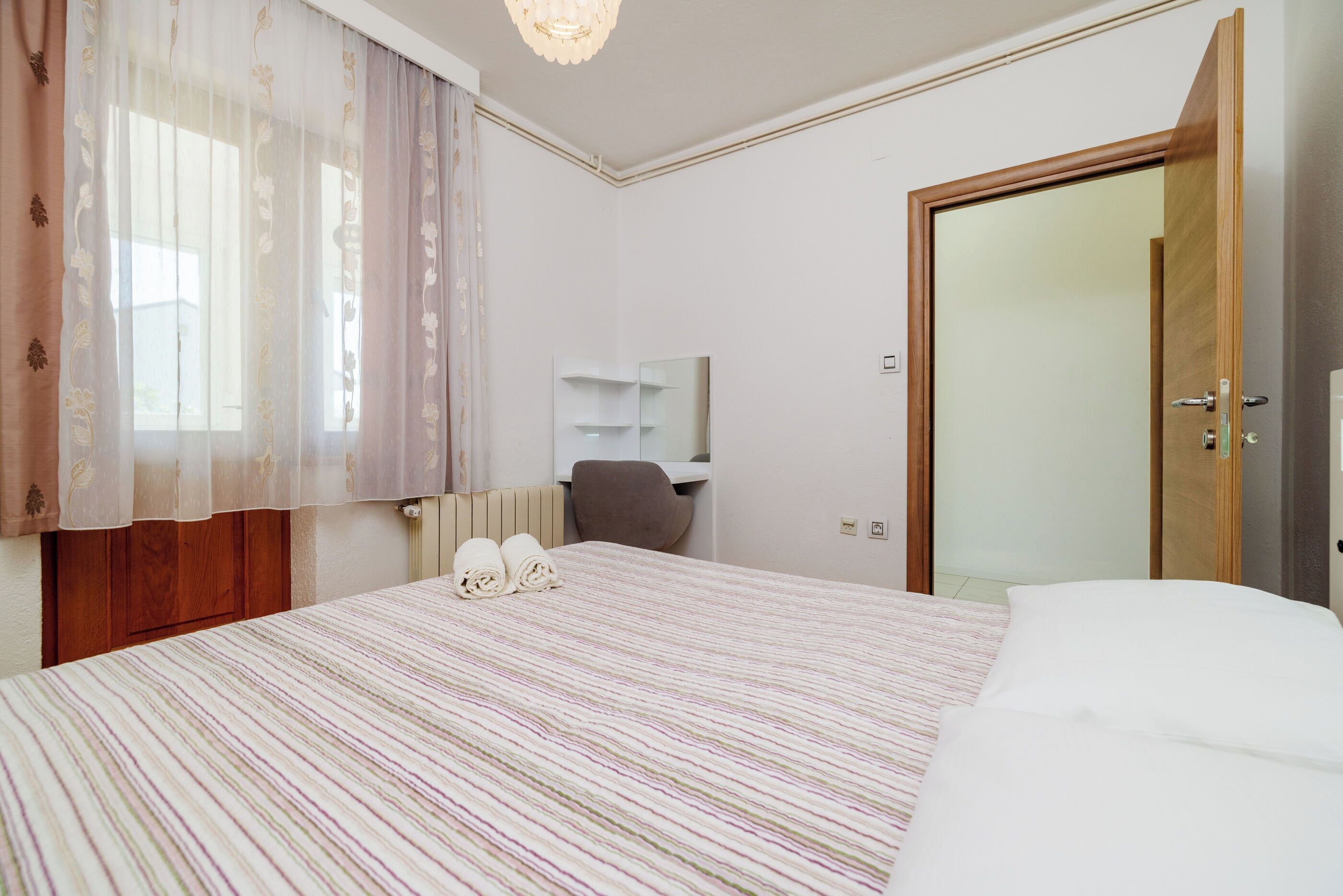 Una habitación de hotel con una cama, una silla, un armario de madera, un espejo y una puerta.