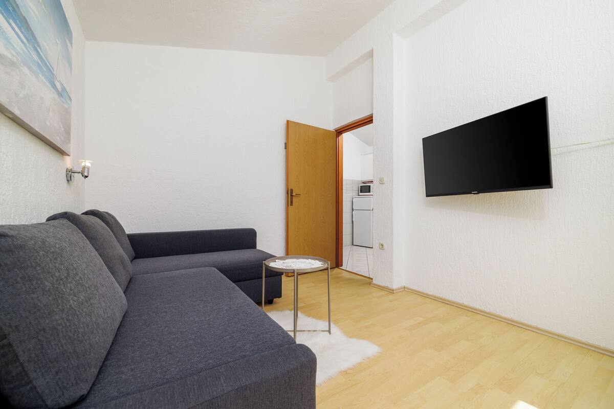 Una sala de estar moderna con un sofá seccional gris, una mesita redonda y un televisor de pantalla plana montado en la pared.
