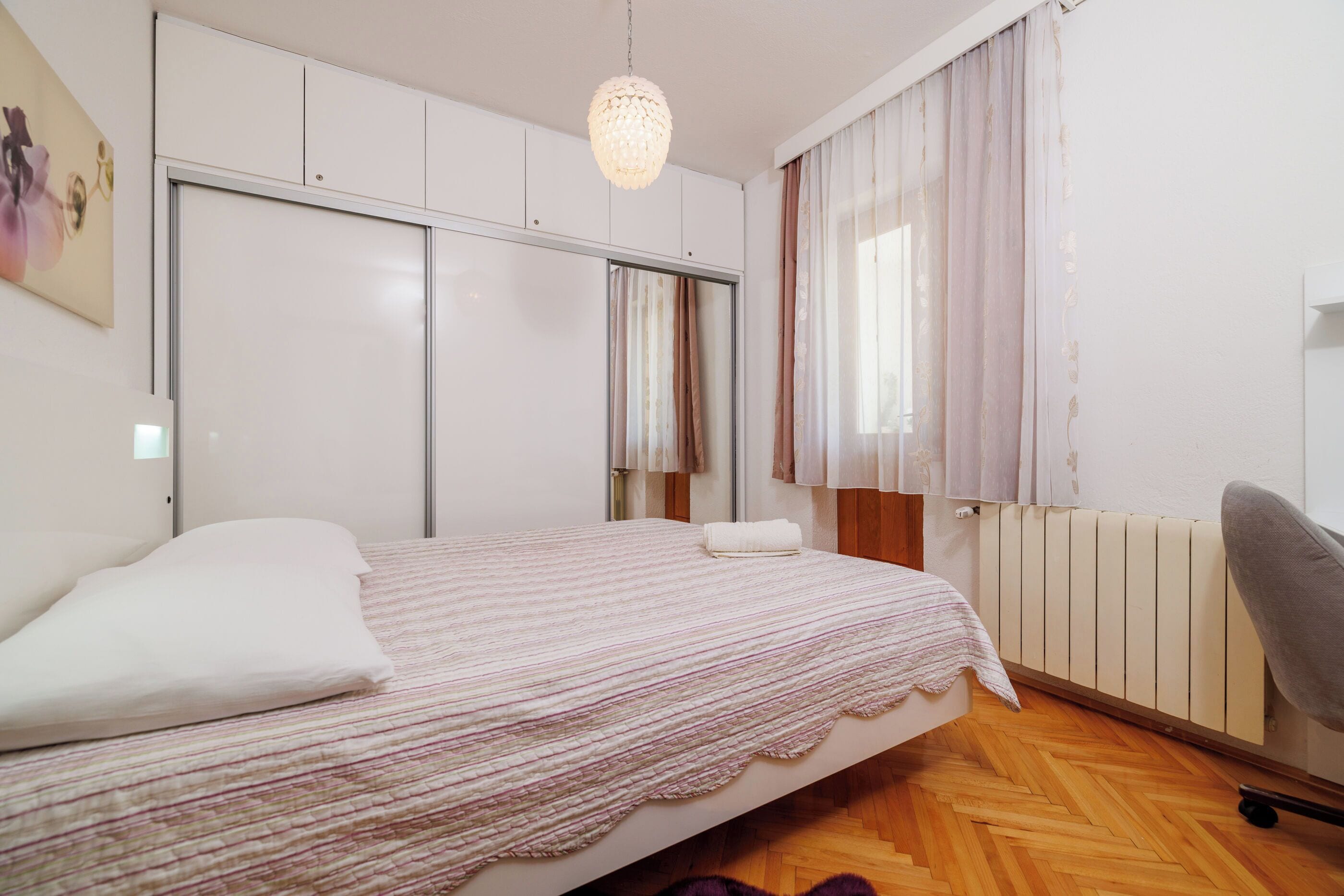 A bedroom with a bed, a chair, a radiator, and a window with curtains.