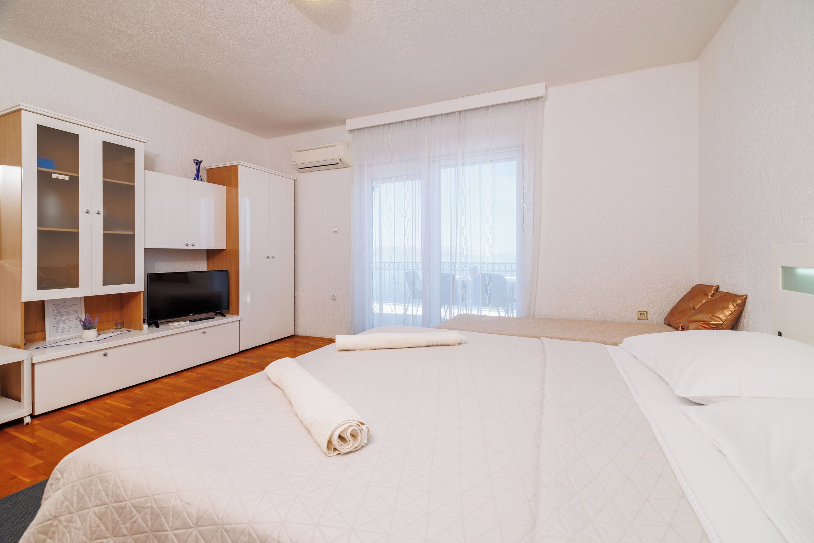 Habitación de hotel con una cama grande, un televisor en un mueble y una ventana con cortinas translúcidas.
