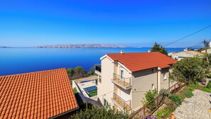 A coastal building with a red-tiled roof, a swimming pool, and a view of the sea.