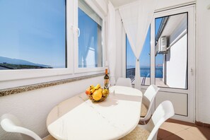 Un balcon avec une table, des chaises, un panier de fruits et une bouteille de vin.
