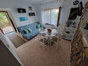 Ein gemütliches Wohnzimmer mit einem blau gemusterten Sofa, einem Esstisch mit Stühlen und einem kleinen Beistelltisch mit einem Korb.